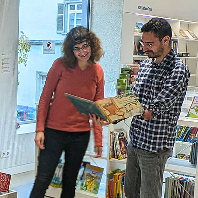 Eine Frau und ein Mann stehen inmitten einer Kinderbibliothek und schauen in ein Buch.