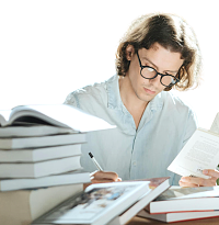 eine Person mit Brille sitzt zwischen vielen Büchern und ist in die Lektüre vertieft