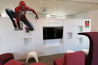 im Vordergrund dunkelrote Sessel, dahinter ein großer Bildschirm, Wände in weiß gehalten, Deko: Spider-Man-Figur