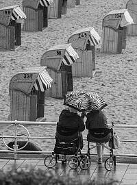 Schwarz-Weiß-Fotografie von einem Strand. Man sieht Strandkörbe und zwei Personen mit Rollatoren. 