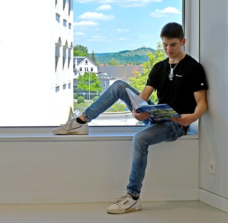 Junger Mann sitzt auf einer Fensterbank und liest ein Buch Quelle: Steffen Schlüter