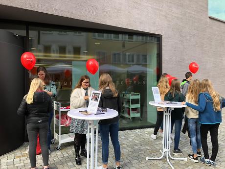 Eine Gruppe von Menschen stehen an Stehtischen zusammen. Rote Luftballons werden aufgeblasen. Quelle: Stadtbibliothek Rottenburg